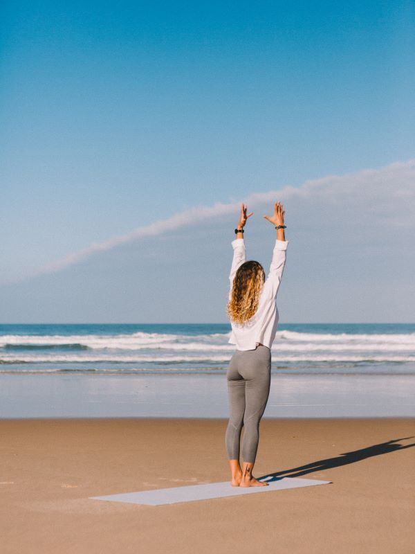 Frau am Strand auf nachhaltiger Yogamatte stehend mit Meerblick